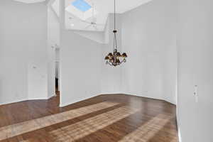 Unfurnished dining area featuring a skylight, dark wood-style floors, suspended lighting, and lofted ceiling