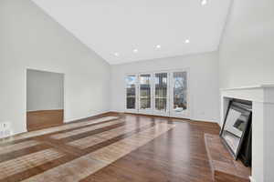 Unfurnished living room featuring dark wood finished floors, vaulted ceiling, a glass covered fireplace, and recessed lighting