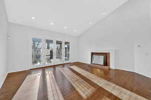 Unfurnished living room featuring lofted ceiling, a fireplace with raised hearth, dark wood-style flooring, french doors, and recessed lighting