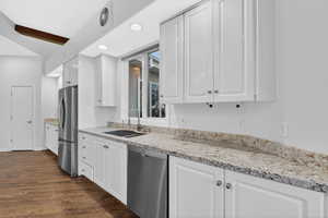 Kitchen with light stone countertops, white cabinets, stainless steel appliances, dark wood-style floors, and recessed lighting