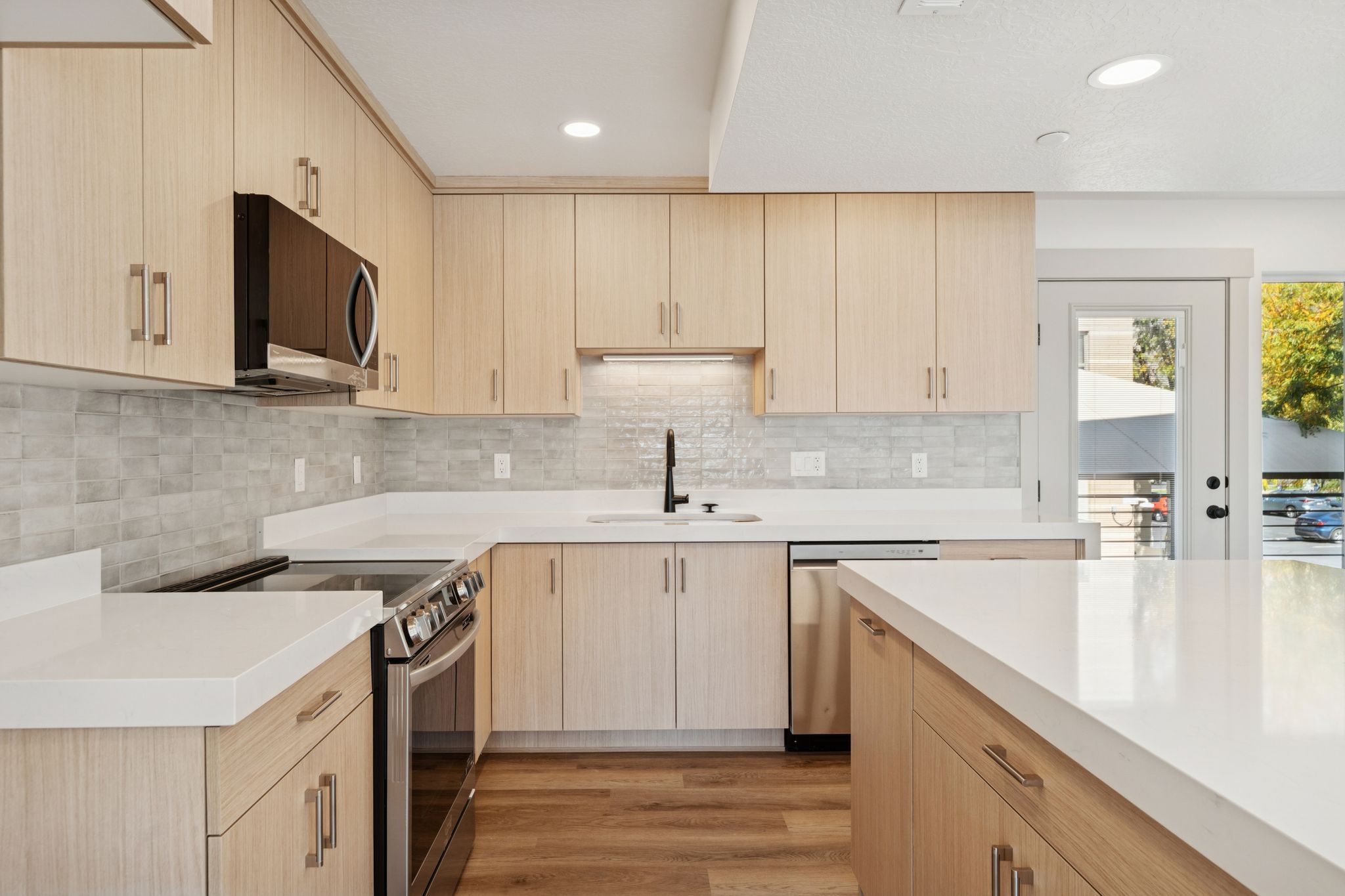 Kitchen featuring light wood finish cabinets, stainless steel appliances, light wood-style flooring, light stone counters, and backsplash