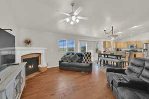 Living room with lofted ceiling, a chandelier, ceiling fan, a tile fireplace, and light wood finished floors