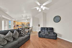 Living area featuring lofted ceiling, light wood-style floors, suspended lighting, and a ceiling fan