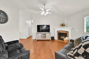 Living area featuring light wood-style flooring, a tile fireplace, lofted ceiling, and a ceiling fan