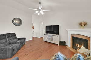 Living area with vaulted ceiling, hardwood / wood-style flooring, a fireplace, and ceiling fan