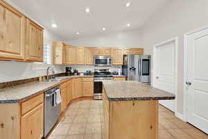 Kitchen with a kitchen island, lofted ceiling, stainless steel appliances, light wood finish cabinetry, and recessed lighting