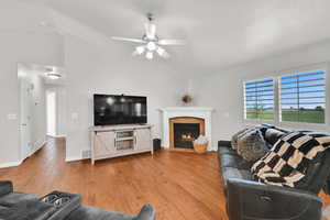 Living area with light wood-style flooring, lofted ceiling, a fireplace with flush hearth, and ceiling fan