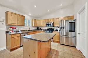 Kitchen featuring stainless steel appliances, a kitchen island, vaulted ceiling, dark countertops, and light wood finish cabinetry