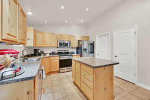 Kitchen with light wood finish cabinetry, a kitchen island, stainless steel appliances, vaulted ceiling, and light tile patterned floors