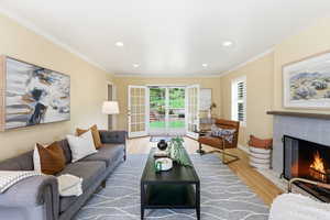 Living room with light wood finished floors, a tile fireplace, recessed lighting, and ornamental molding