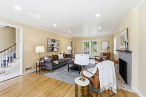 Living room featuring light wood finished floors, ornamental molding, recessed lighting, and a brick fireplace