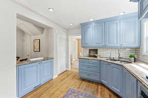 Kitchen featuring blue cabinets, light stone counters, light wood-type flooring, decorative backsplash, and recessed lighting