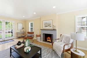 Living room featuring light wood-style floors, a tiled fireplace, crown molding, and recessed lighting