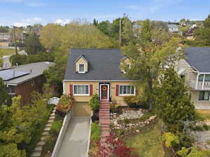 Cape cod home with roof with shingles, a garage, driveway, and a residential view