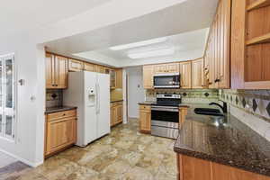 Kitchen with stainless steel appliances, glass fronted cabinets, dark stone countertops, a textured ceiling, and stone finish floors