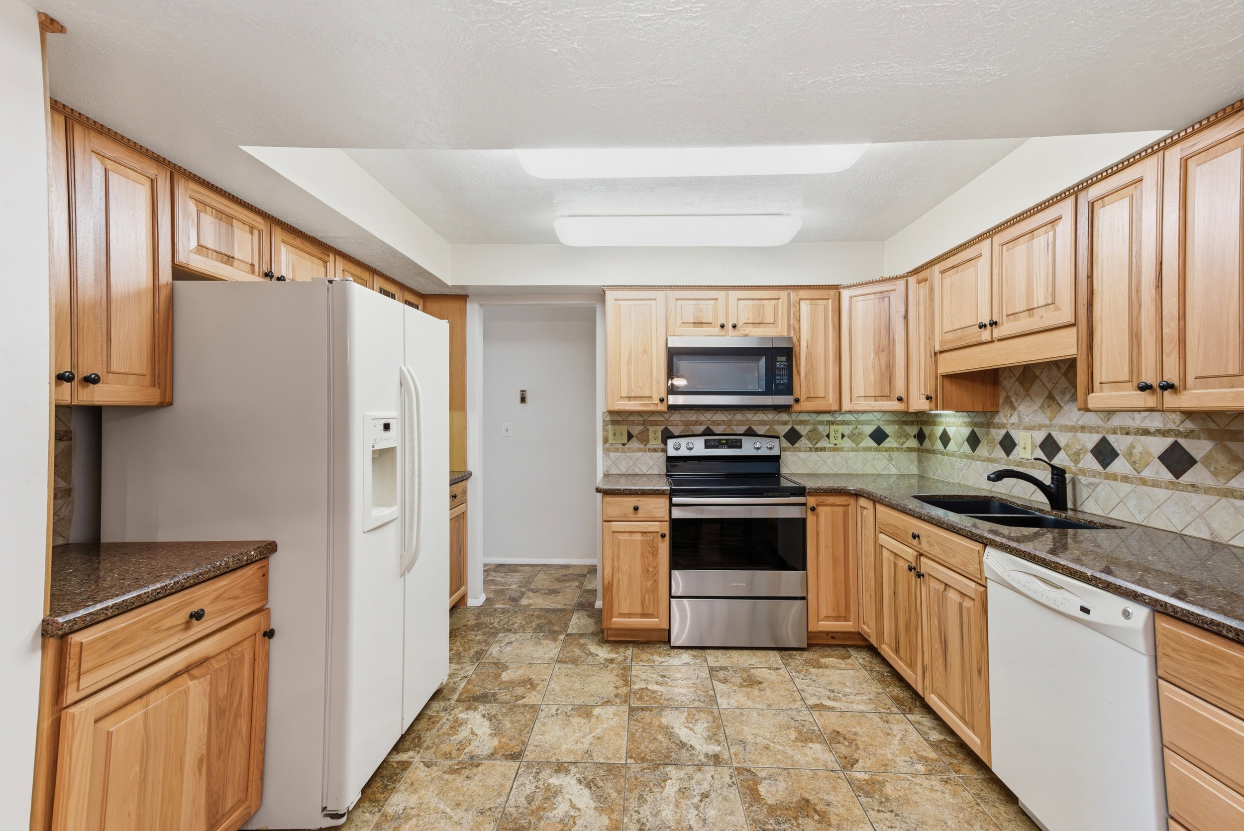 Kitchen with stainless steel appliances, dark stone countertops, light wood finish cabinets, and decorative backsplash