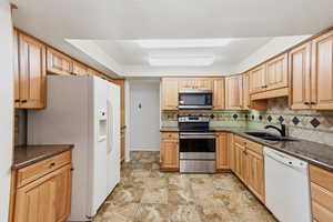 Kitchen with stainless steel appliances, dark stone countertops, light wood finish cabinets, and decorative backsplash