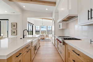 Two tone kitchen with a chandelier, stainless steel gas cooktop, light stone countertops, light wood-style flooring, and a large island