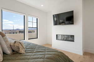 Bedroom with light wood-type flooring, recessed lighting, and a glass covered fireplace