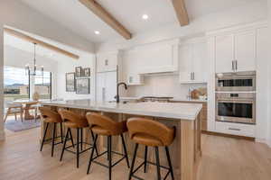 Kitchen with light wood-style flooring, beamed ceiling, two tone color scheme, a breakfast bar, and decorative backsplash