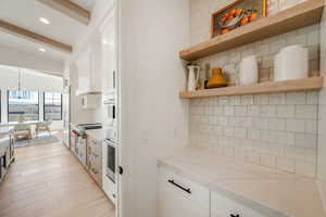 Kitchen with tasteful backsplash, open shelves, white cabinets, beam ceiling, and light wood-style flooring