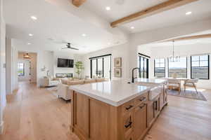 Kitchen with hanging lights, open floor plan, beamed ceiling, an island with sink, and light wood-type flooring