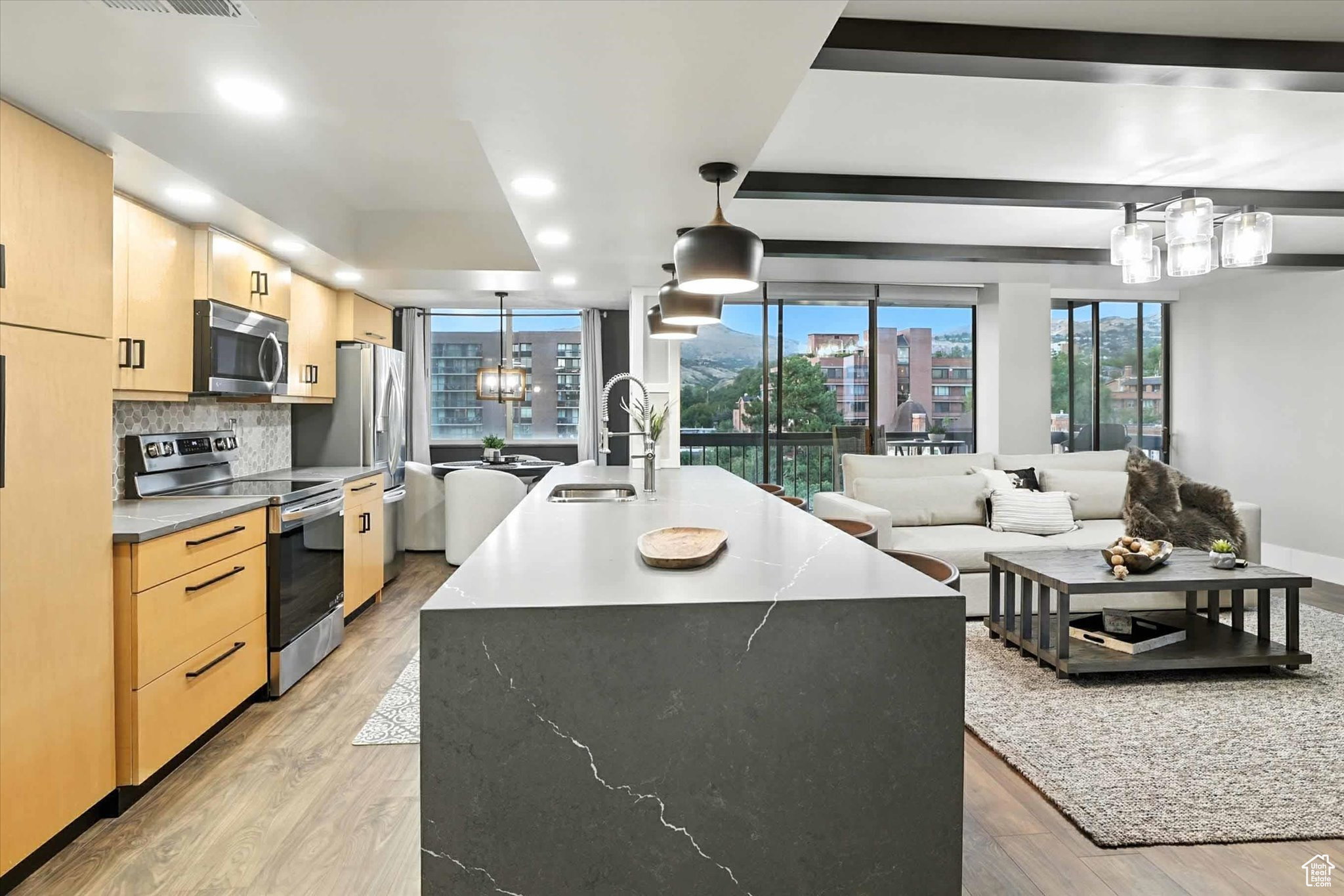 Kitchen featuring light brown cabinetry, stainless steel appliances, a center island with sink, and a chandelier