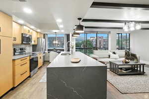 Kitchen featuring light brown cabinetry, stainless steel appliances, a center island with sink, and a chandelier