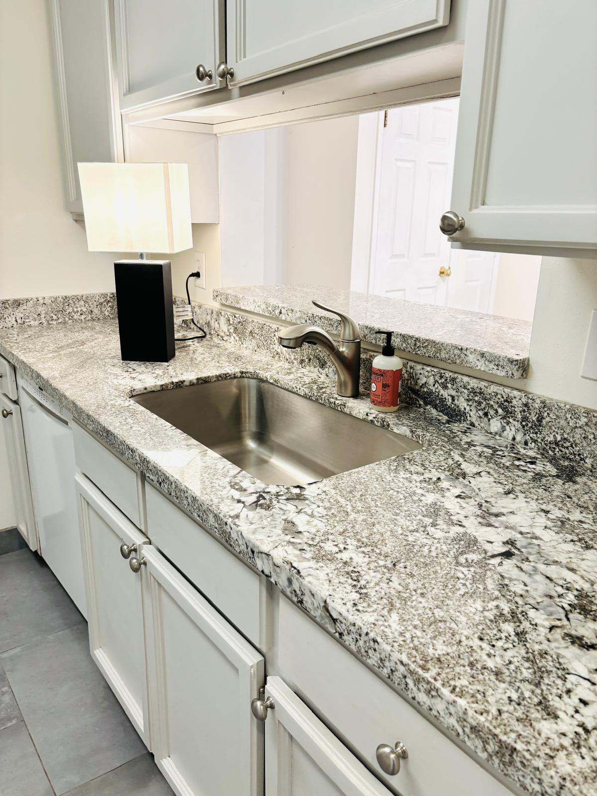 Kitchen with white cabinets, light stone countertops, and white dishwasher