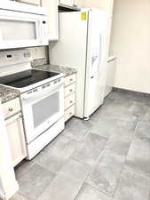 Kitchen featuring white appliances, white cabinetry, light tile patterned floors, and light stone countertops