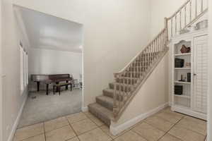 Stairs with carpet flooring, tile patterned floors, and ornamental molding