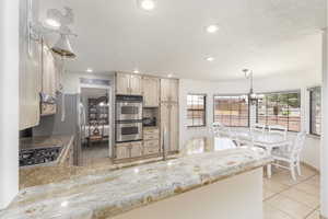 Kitchen with light tile patterned flooring, suspended lighting, stainless steel appliances, a textured ceiling, and a peninsula