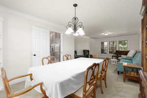 Dining room with crown molding, light colored carpet, and a chandelier