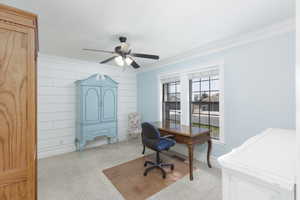 Home office with light colored carpet, crown molding, ceiling fan, and wood walls