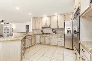 Kitchen featuring a peninsula, light stone counters, stainless steel appliances, crown molding, and a ceiling fan