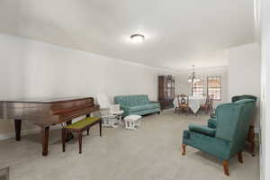 Living area with ornamental molding, suspended lighting, and light carpet