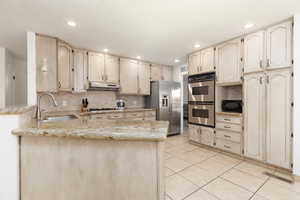 Kitchen with a peninsula, light stone countertops, stainless steel appliances, light wood finish cabinets, and recessed lighting
