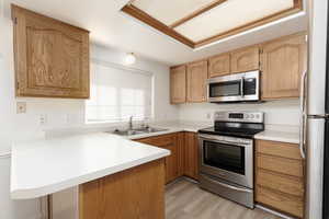Kitchen with stainless steel appliances, light countertops, light wood-type flooring, and a peninsula