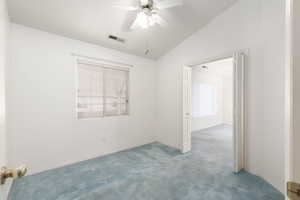 Carpeted empty room featuring vaulted ceiling and ceiling fan