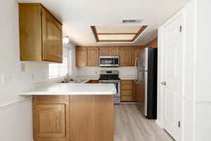 Kitchen with light countertops, stainless steel appliances, a peninsula, wood finish cabinets, and light wood finished floors