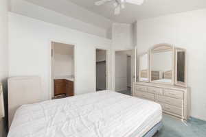 Bedroom featuring carpet, a spacious closet, a ceiling fan, ensuite bath, and vaulted ceiling