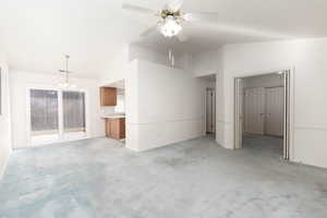 Unfurnished living room featuring lofted ceiling, ceiling fan, a chandelier, and light carpet