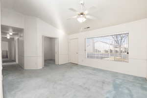 Unfurnished living room featuring a ceiling fan, vaulted ceiling, and light colored carpet