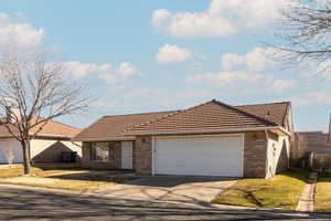 View of front facade with concrete driveway, a garage, brick siding, a front yard, and a tile roof