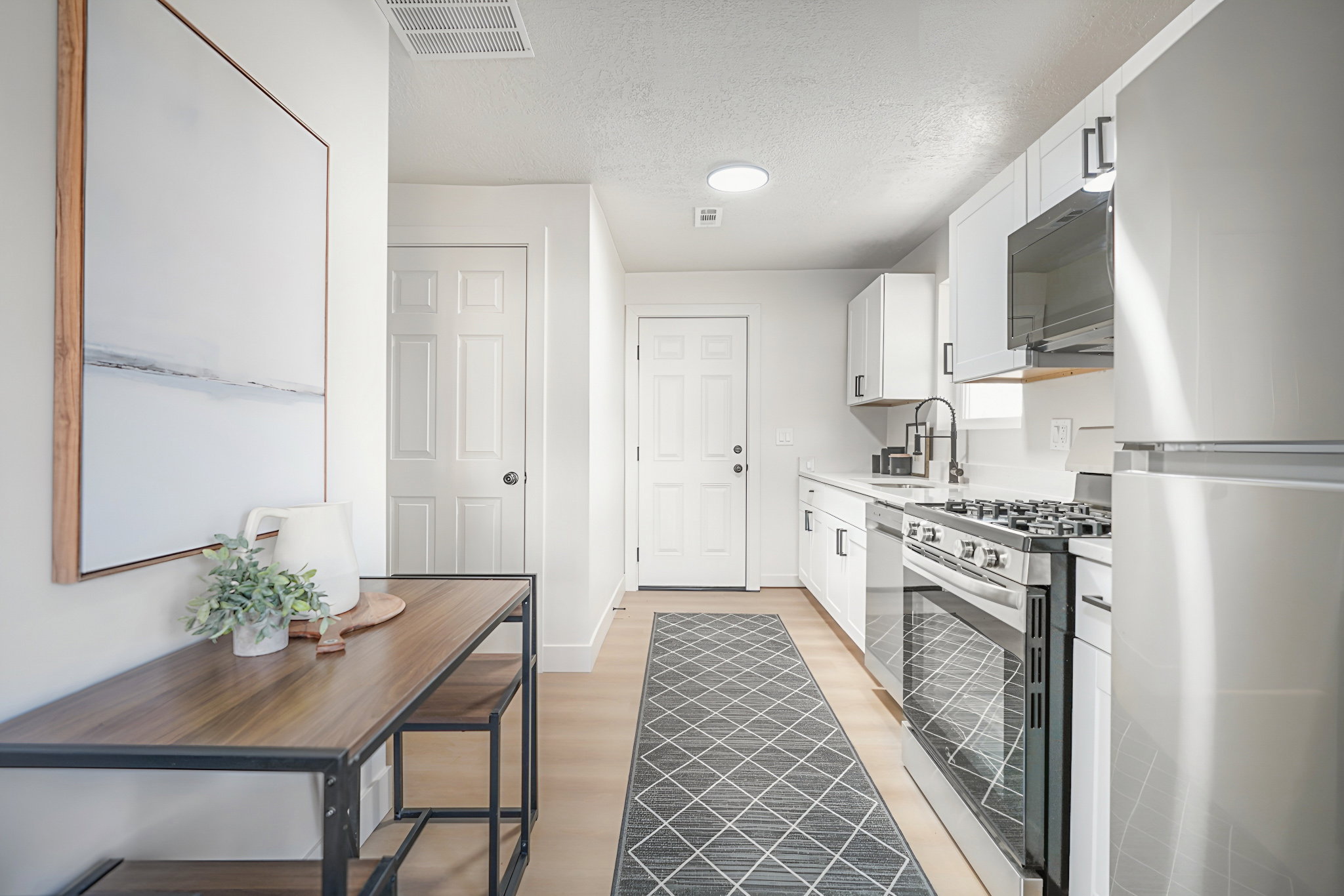 Kitchen featuring stainless steel appliances, white cabinets, a textured ceiling, and light wood-style flooring