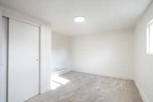 Empty room featuring light colored carpet and a baseboard heating unit
