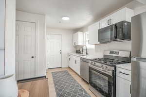 Kitchen with stainless steel appliances, light countertops, white cabinets, a textured ceiling, and light wood finished floors