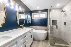 Full bathroom featuring a soaking tub, a shower stall, double vanity, tile walls, and wainscoting