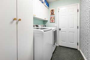 Laundry room with cabinet space, independent washer and dryer, and dark tile patterned flooring