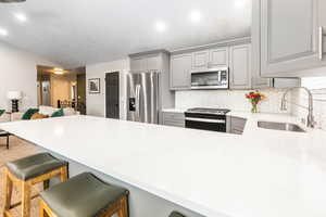 Kitchen featuring gray cabinetry, stainless steel appliances, a breakfast bar area, and a peninsula